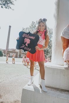 a girl in a pink dress holding a welcome home sign and standing on some steps