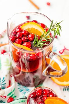 a pitcher filled with cranberry punch and garnished with orange slices, rosemary and lemon wedges