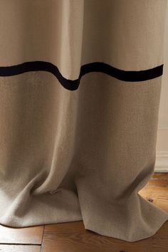 a close up view of a curtain with black stripes on the bottom and side, in front of a wooden floor