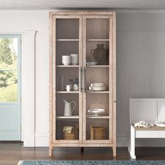 a wooden cabinet with glass doors in a living room next to a white bench and blue rug