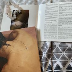 an open book sitting on top of a bed next to two pictures and a pillow