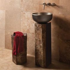 a bathroom sink sitting on top of a stone block next to a red towel and a faucet