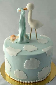 a blue cake with white clouds and a stork figurine on top