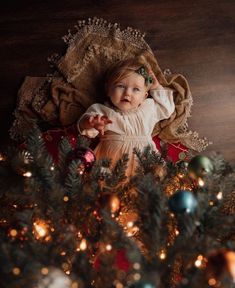 a baby laying on top of a christmas tree next to a pile of ornaments and lights