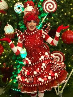 a woman in a red dress standing next to a christmas tree with lollipops on it