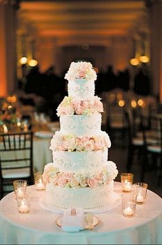 a wedding cake sitting on top of a white table covered in flowers and lit candles