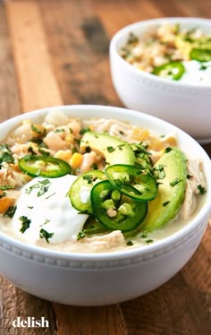 two white bowls filled with soup on top of a wooden table and topped with cucumbers