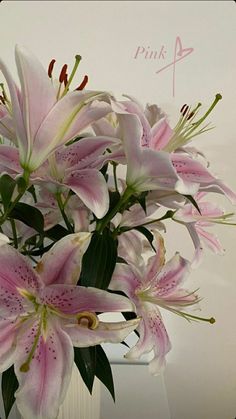 a vase filled with pink lilies on top of a white tablecloth covered table