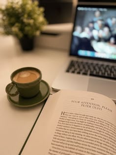 an open book with a cup of coffee next to it and a laptop on the table