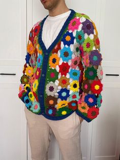 a man standing in front of a white door wearing a colorful crochet sweater