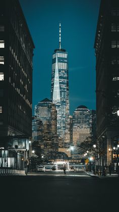 the city skyline is lit up at night with skyscrapers in the foreground and people walking on the sidewalk