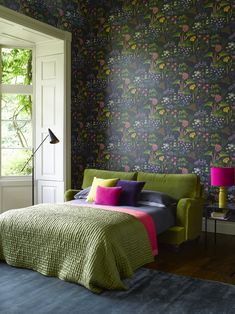 a green bed in a bedroom next to a wall with flowers on it and pink lamps