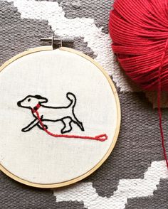 a red ball of yarn sitting next to a white and black dog embroideryed on a hoop