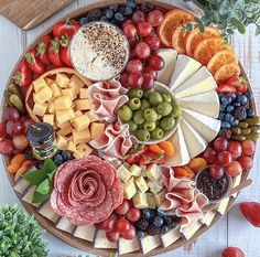 an assortment of cheeses, meats and fruit on a platter with flowers