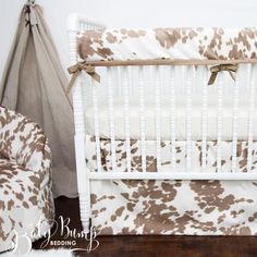 a white crib with brown and white bedding next to a baby's chair