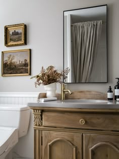 a bathroom with a sink, toilet and paintings on the wall above it's mirror