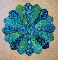 a blue and green circular piece of art made from fabric on a beige carpeted floor