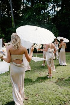 a bride and her bridal party walking in the grass with their umbrellas open