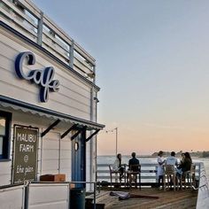 people are sitting at tables on the dock by the water and cafe is open for business