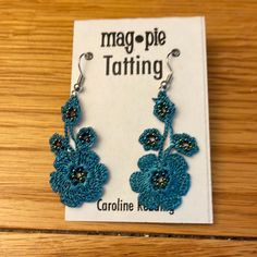 a pair of earrings with blue flowers on them sitting on top of a wooden table