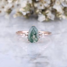 a green and white diamond ring sitting on top of a marble table with flowers in the background