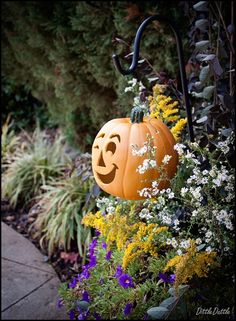 a jack o lantern pumpkin sitting on top of a planter next to some flowers