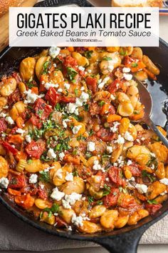 a skillet filled with pasta and vegetables on top of a wooden cutting board next to bread