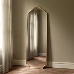 a large mirror sitting on top of a hard wood floor next to a white curtain