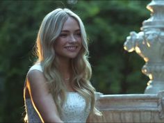 a beautiful blonde woman standing next to a fountain