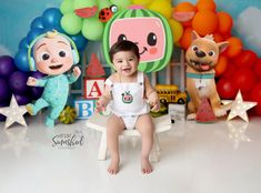 a baby sitting on a chair in front of balloons and stuffed animals with the backdrop behind him