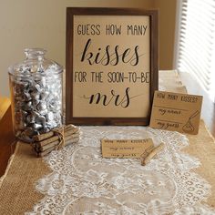 a table topped with lots of candy next to a wooden sign that says guess how many kisses for the son - to - be mes