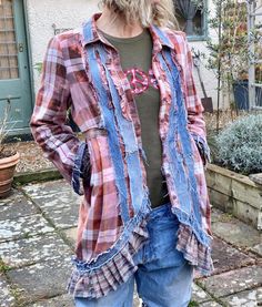 a woman standing in front of a house wearing jeans and a plaid shirt with ruffles