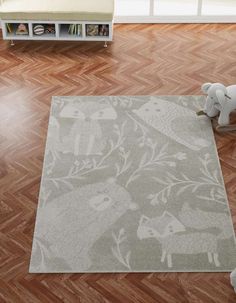 a teddy bear sitting on top of a wooden floor next to a rug with animals