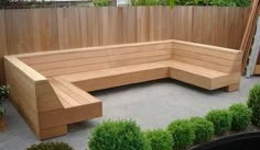 a wooden bench sitting on top of a cement ground next to bushes and shrubbery