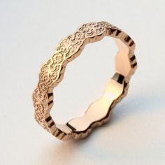 a gold wedding ring with intricate designs on the outside and inside, sitting on a white surface