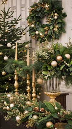 christmas wreaths and greenery on display in front of a white wall with gold candlesticks