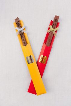 two red and yellow pencils with gold writing on them sitting next to each other