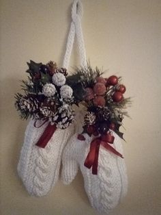 two white knit mittens hanging from a wall with christmas decorations on top of them