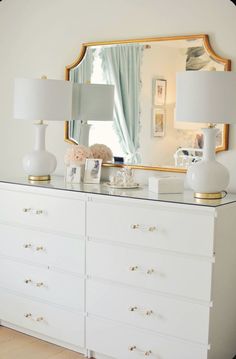 a white dresser topped with two lamps and a mirror