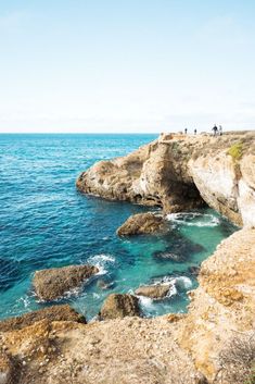 people are standing on the cliff above the water