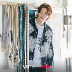 a young man standing in front of a wall with many necklaces hanging from it