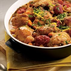 a white bowl filled with meat and vegetables on top of a yellow napkin next to silverware