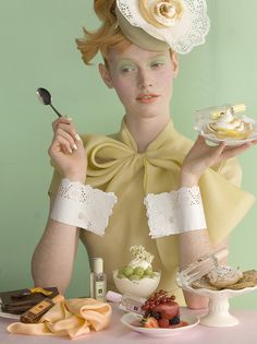 a woman in a yellow dress and hat holding a plate with desserts on it