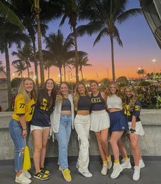 a group of young women standing next to each other in front of palm trees at sunset