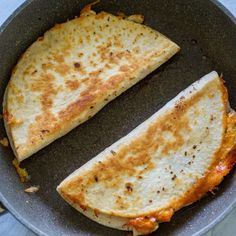 two quesadillas in a frying pan on the stove top, one cut in half