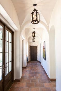 a long hallway with two lamps hanging from it's ceiling and doors leading to another room