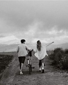 a man and woman walking down a dirt road with their arms in the air while holding hands