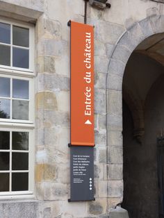 an orange sign hanging from the side of a stone building next to a white door