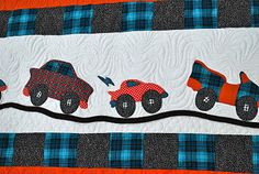 a quilted wall hanging with three cars on it's sides and an orange background