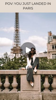 a woman sitting on top of a stone wall next to the eiffel tower